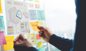 Hand placing sticky notes on a goal planning board during mid-year reflection and goal alignment process